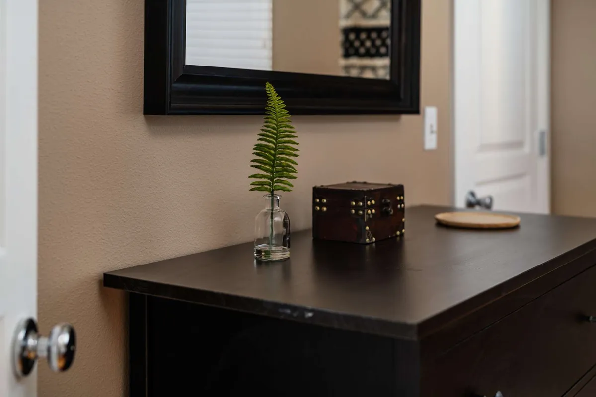 A stylish entryway vignette with a fern in a glass vase, a small wooden box, and a mirror. The scene is calm and welcoming, capturing the moment of arrival and the thoughtful details that set the tone for the home.