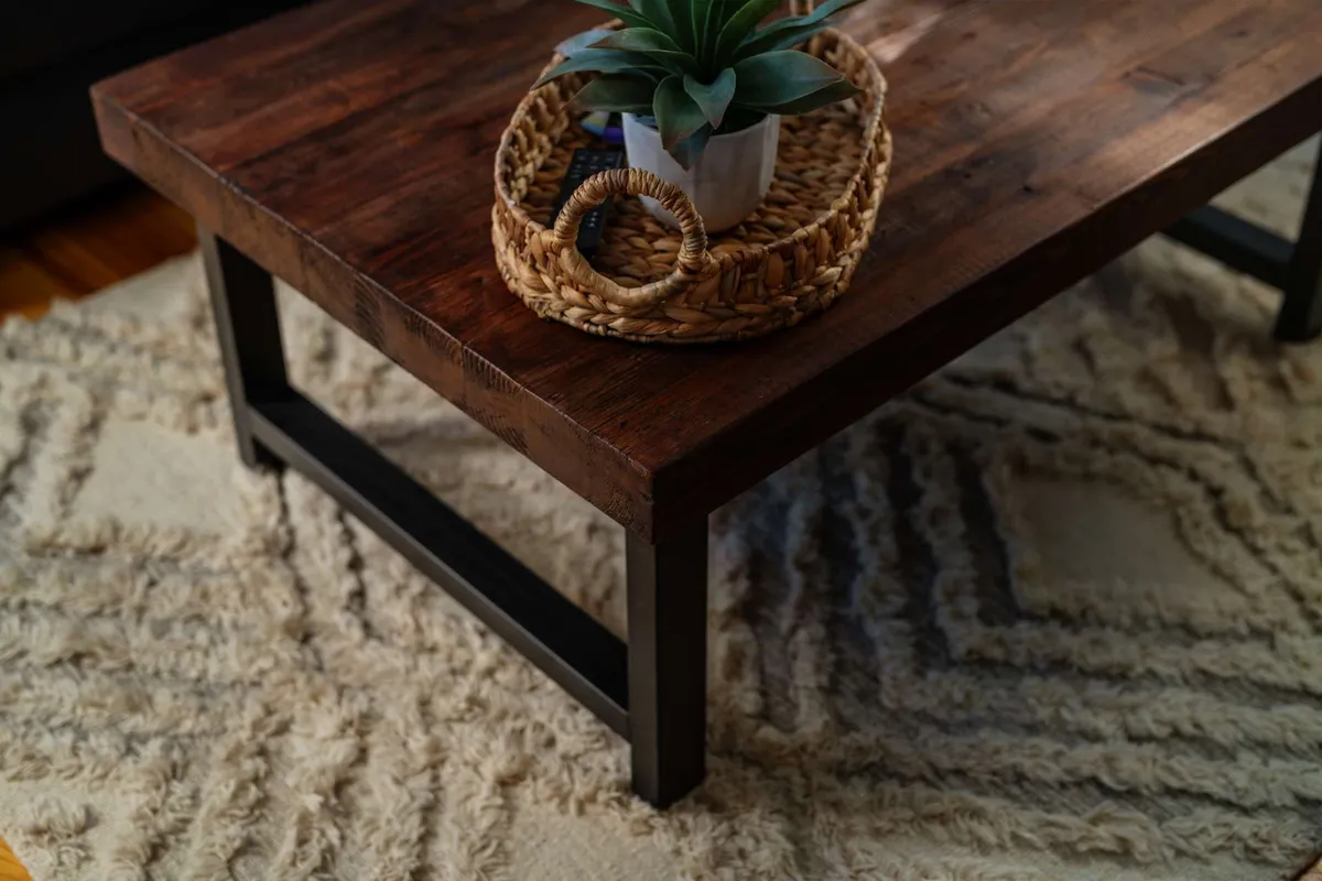 This image centers on a warm, wooden coffee table set with a woven tray and potted plant. The setup is cozy, inviting, and touches on the idea of relaxing after returning from an adventure, with subtle hints of natural textures that evoke the Pacific Northwest environment.