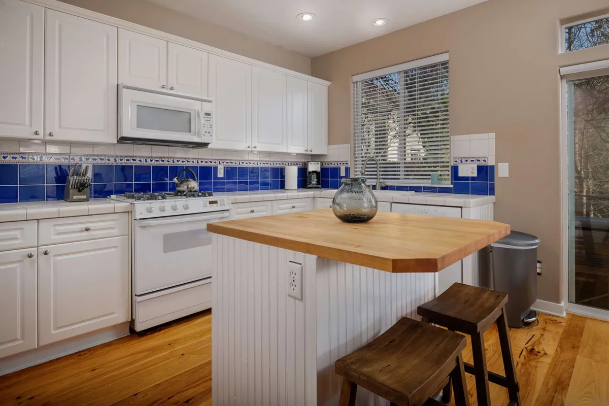 The kitchen island, accented by a blue tile backsplash and wooden stools, forms the heart of a social space ideal for group gatherings. The island is ready for cooking, entertaining, or enjoying a casual breakfast together.