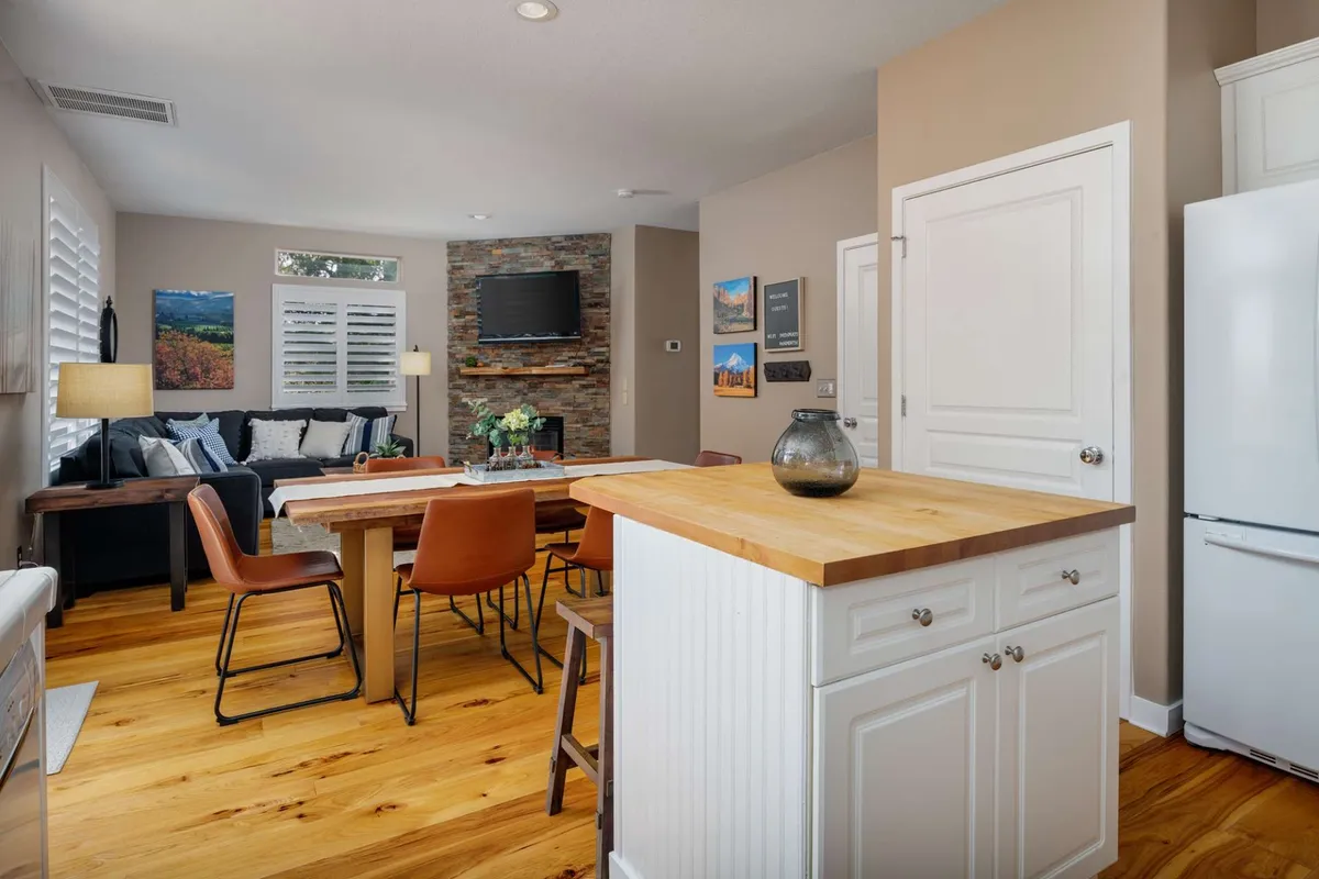 A spacious open-concept living space featuring a kitchen island, a dining table, and a cozy sofa area set against a striking stone feature wall. The areas are seamlessly connected, filled with warm lighting and hints of decor that create a welcoming environment for gatherings.