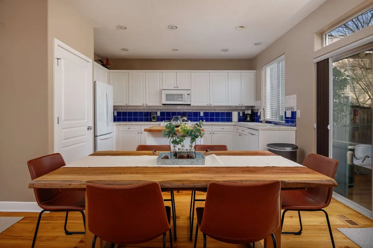 A warm and inviting dining area featuring a dining table set for a family meal, adjacent to stylish kitchen cabinets and a decorative plant. The setup encourages gathering for shared meals or celebrations in a homey atmosphere.