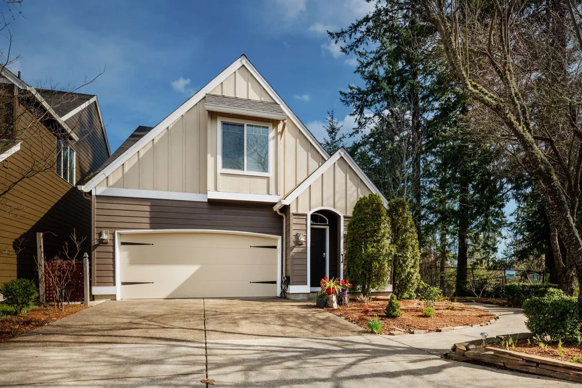 This exterior image captures the welcoming front entrance of Beaverton Creek Cottage, framed by a well-manicured garden and a visible garage door. The inviting, homey atmosphere is underscored by lush landscaping and a pathway leading to the door.