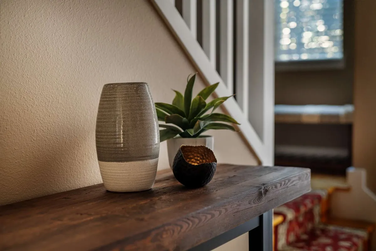 A welcoming vignette featuring gray and black ceramic vases with a green plant on a wooden shelf, likely in an entryway or transitional area. The scene offers a sense of first impressions, blending a natural touch with a modern yet homey feel.
