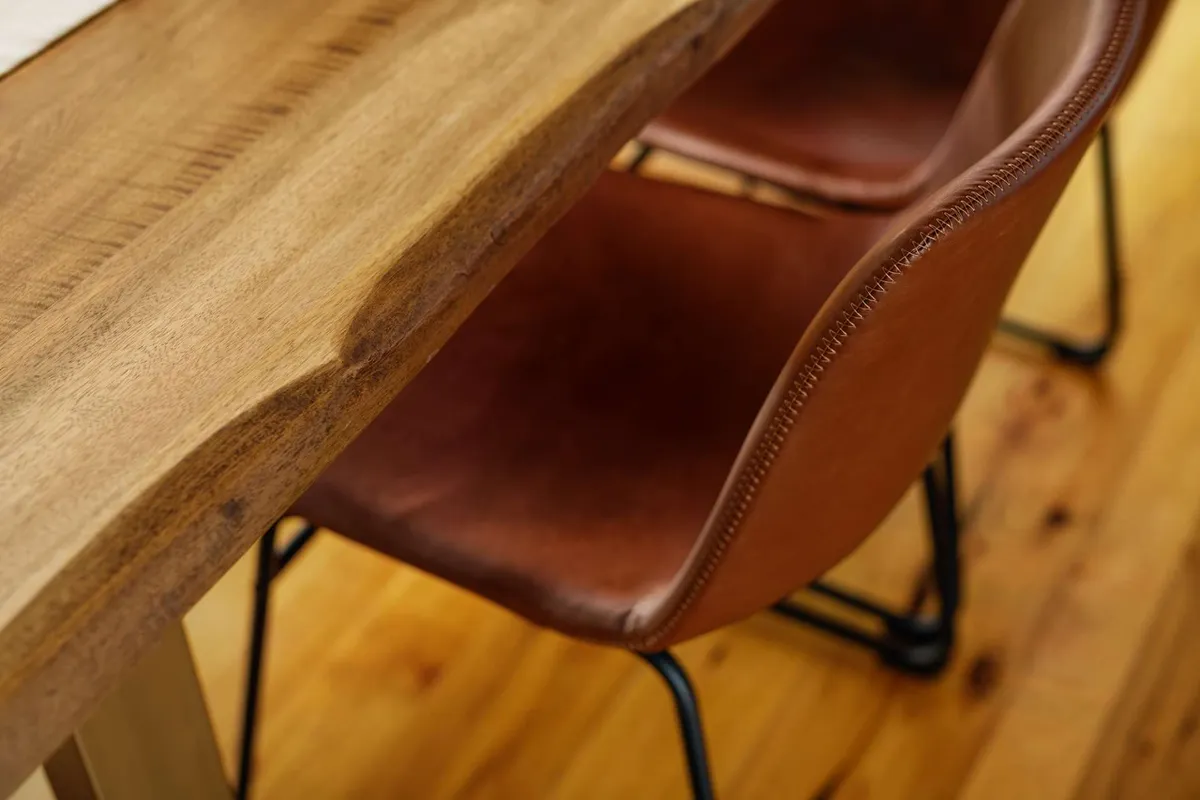 A cozy, well-lit interior scene featuring a wooden table surrounded by leather chairs, offering a space for dining, gathering, or working. The setting is intimate yet functional, suggesting a spot suitable for creative work sessions or family meals.